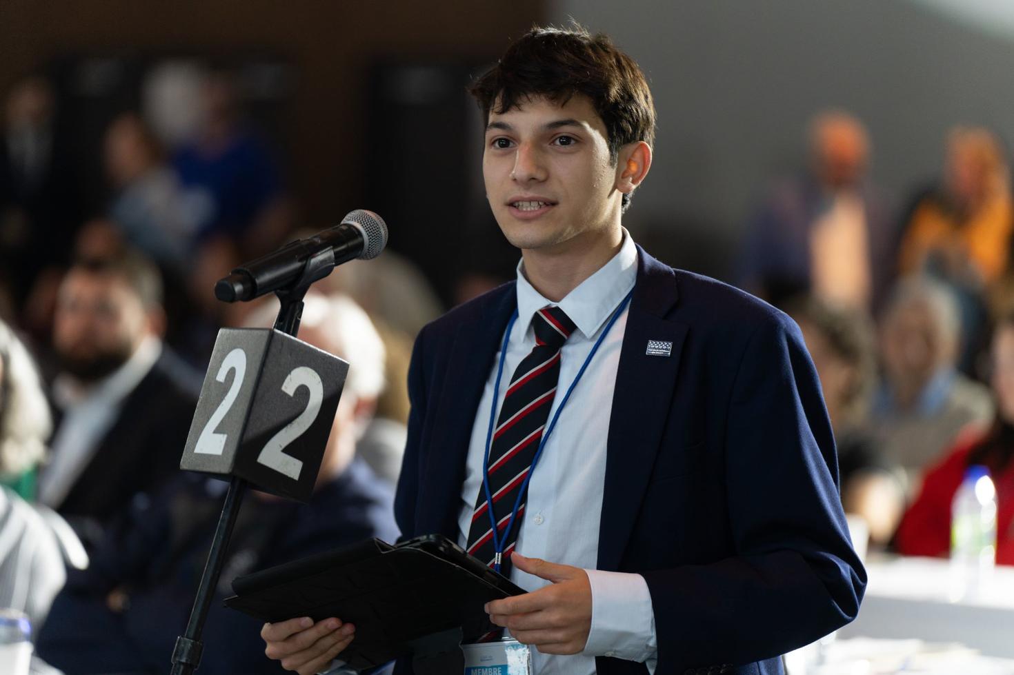 Santiago Proteau-Sanchez speaking in front of a mic.