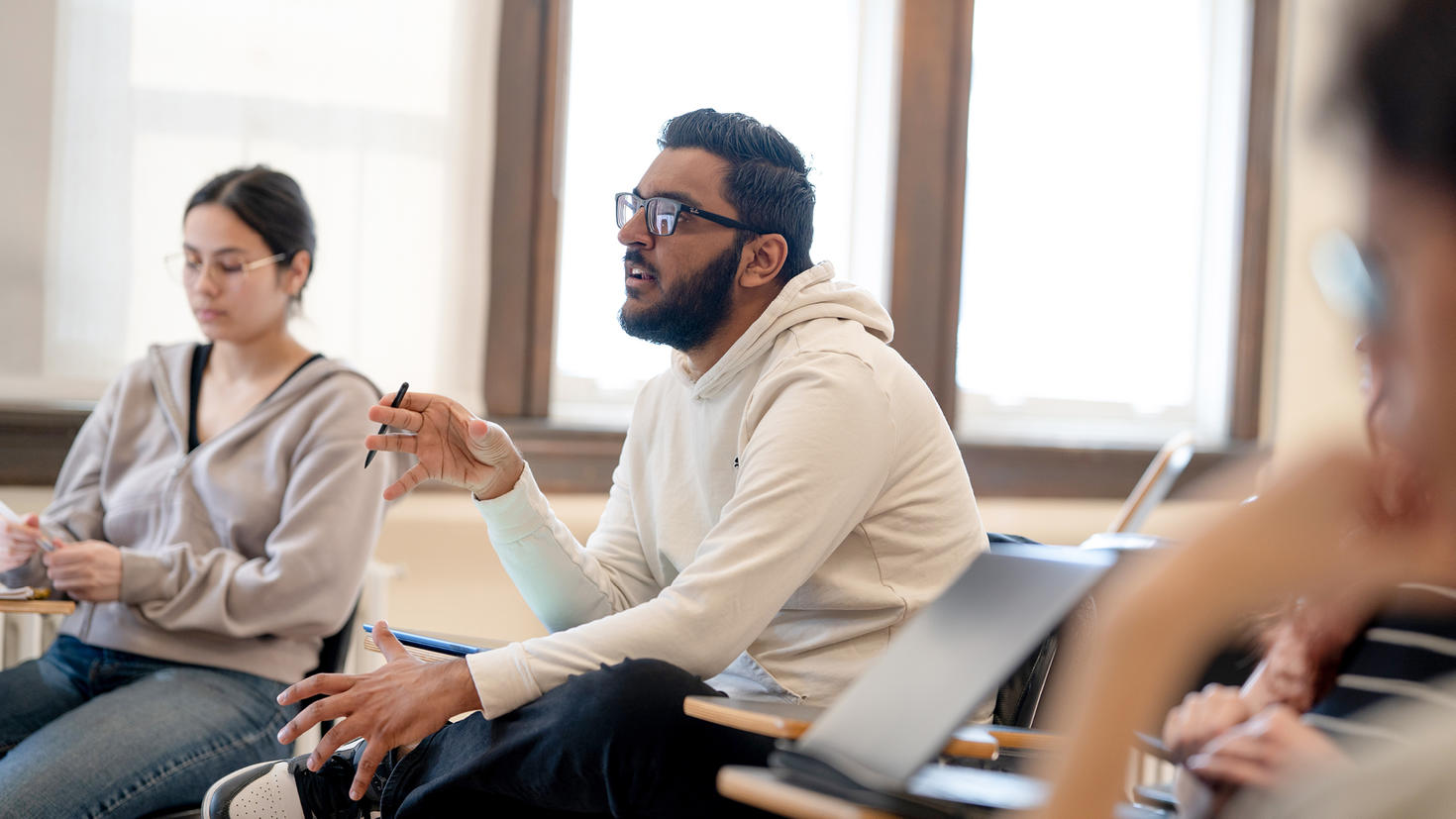 A master’s student talks with classmates inside a classroom.