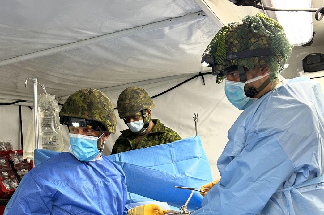 Le Dr Alenko Šakanović effectue une chirurgie sur un patient simulé, vêtu d’une blouse de chirurgien par-dessus un uniforme militaire.