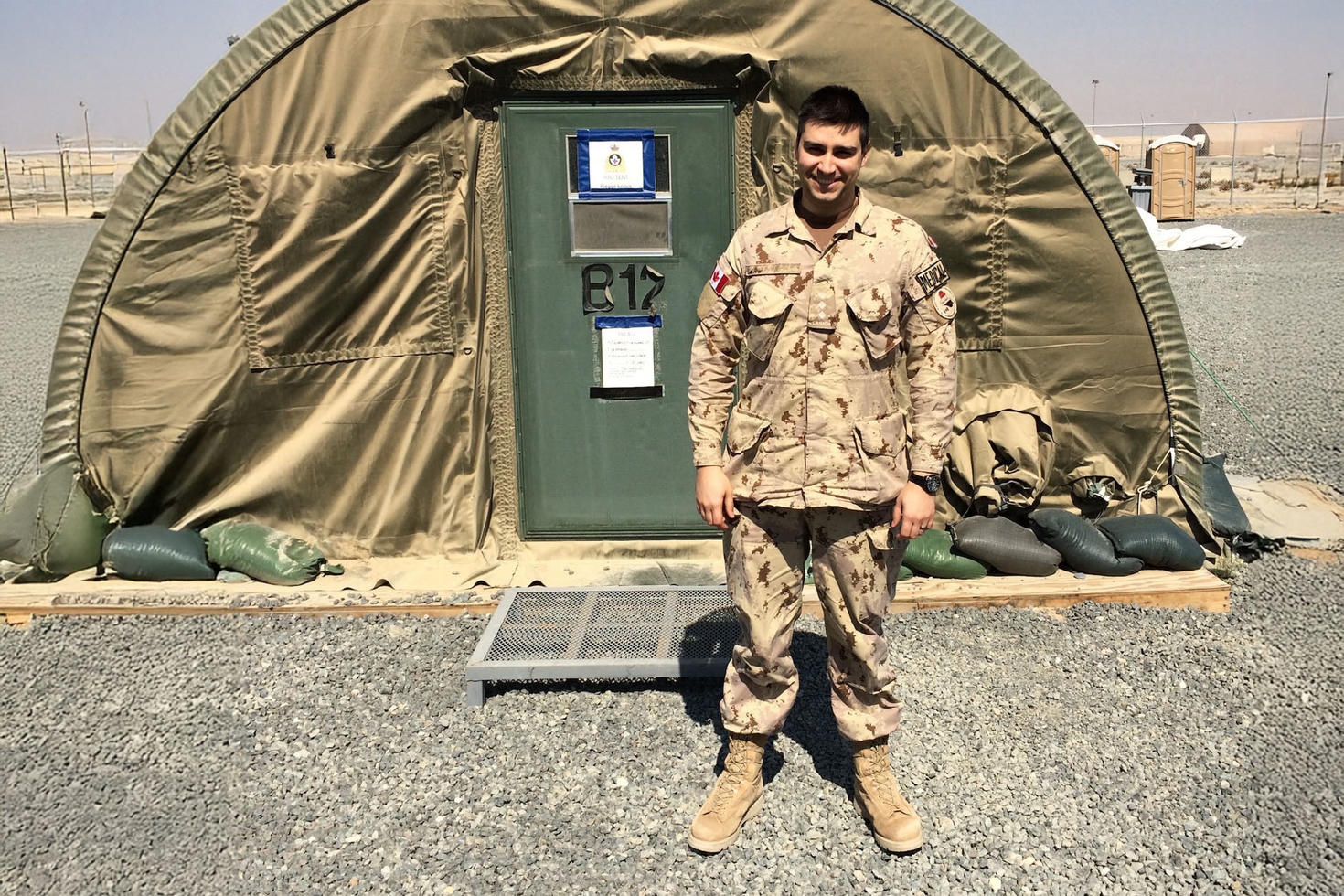 Une personne en uniforme militaire se tient devant une tente militaire.