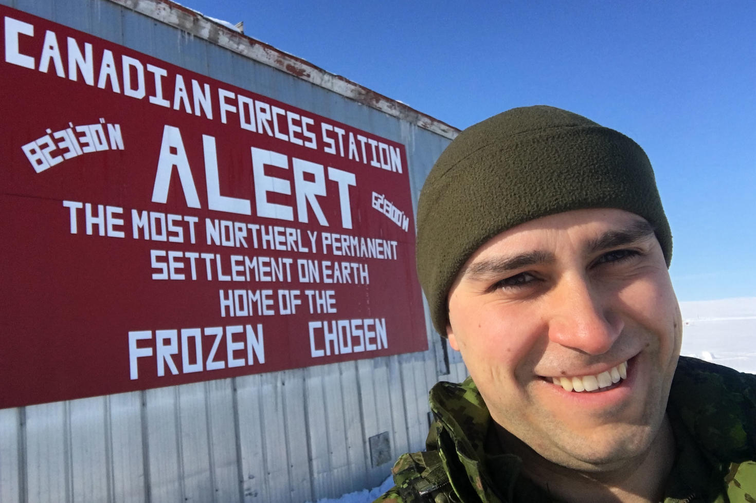 A person in a military uniform in front of an army base sign in the Canadian arctic