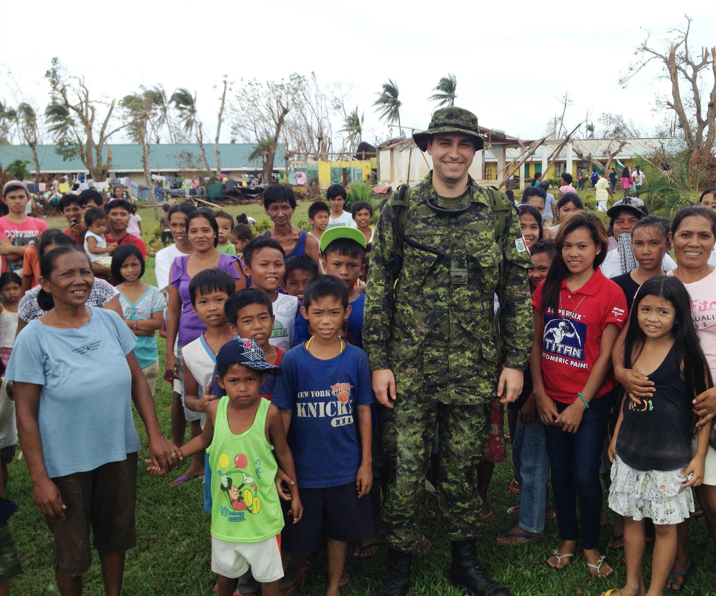 Une personne en uniforme militaire se tient avec des gens dans un village.