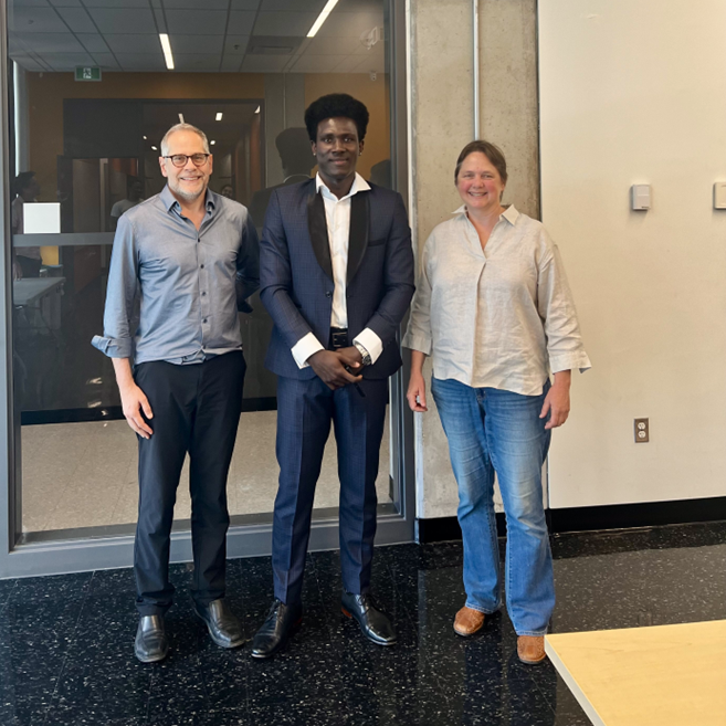 : Professor Robert DeKemp, John Boby Mesadieu and Professor Tanya Schmah standing together indoors in front of a glass-panelled door.