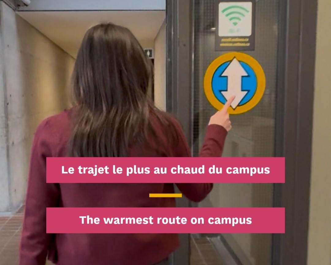 A student points to a warm route sign as she walks through campus buildings.