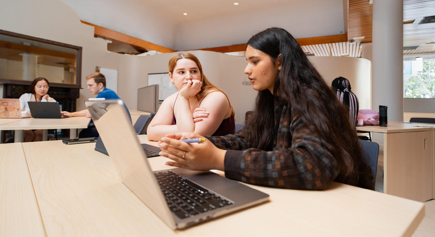 Une mentore en rédaction regarde un ordinateur portable, conseillant une étudiante à côté d'elle.