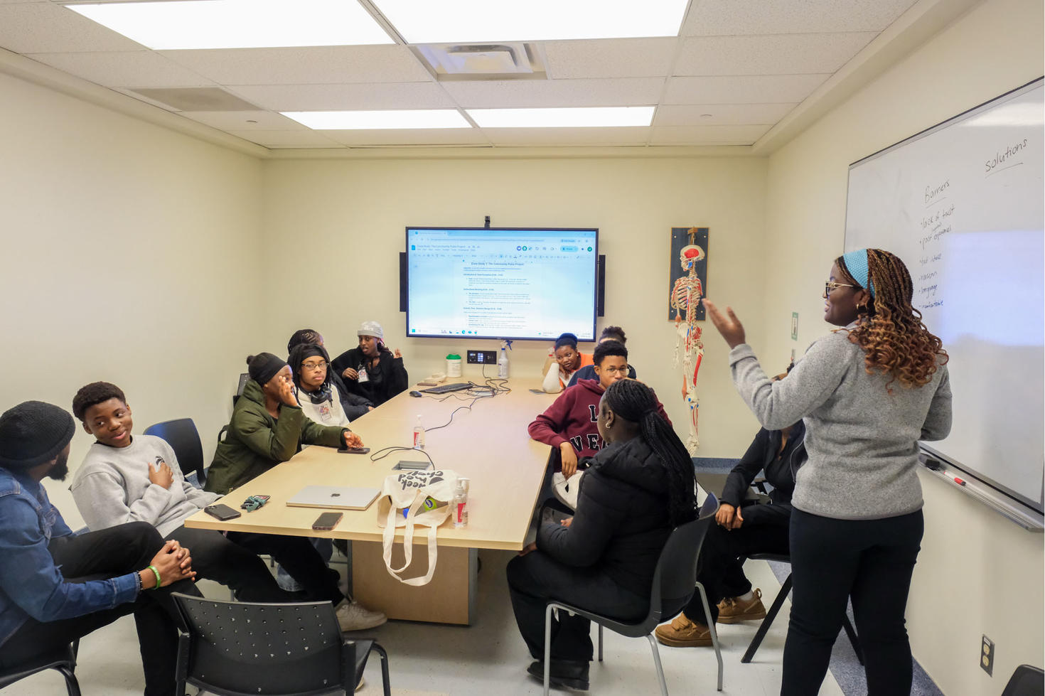 A health professional leads a group of students in discussion around a conference table