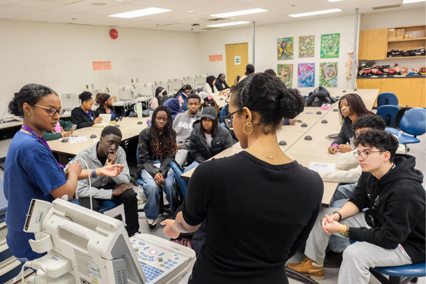 a group of students look on with fascination as health professionals teach them concepts of ultrasound.