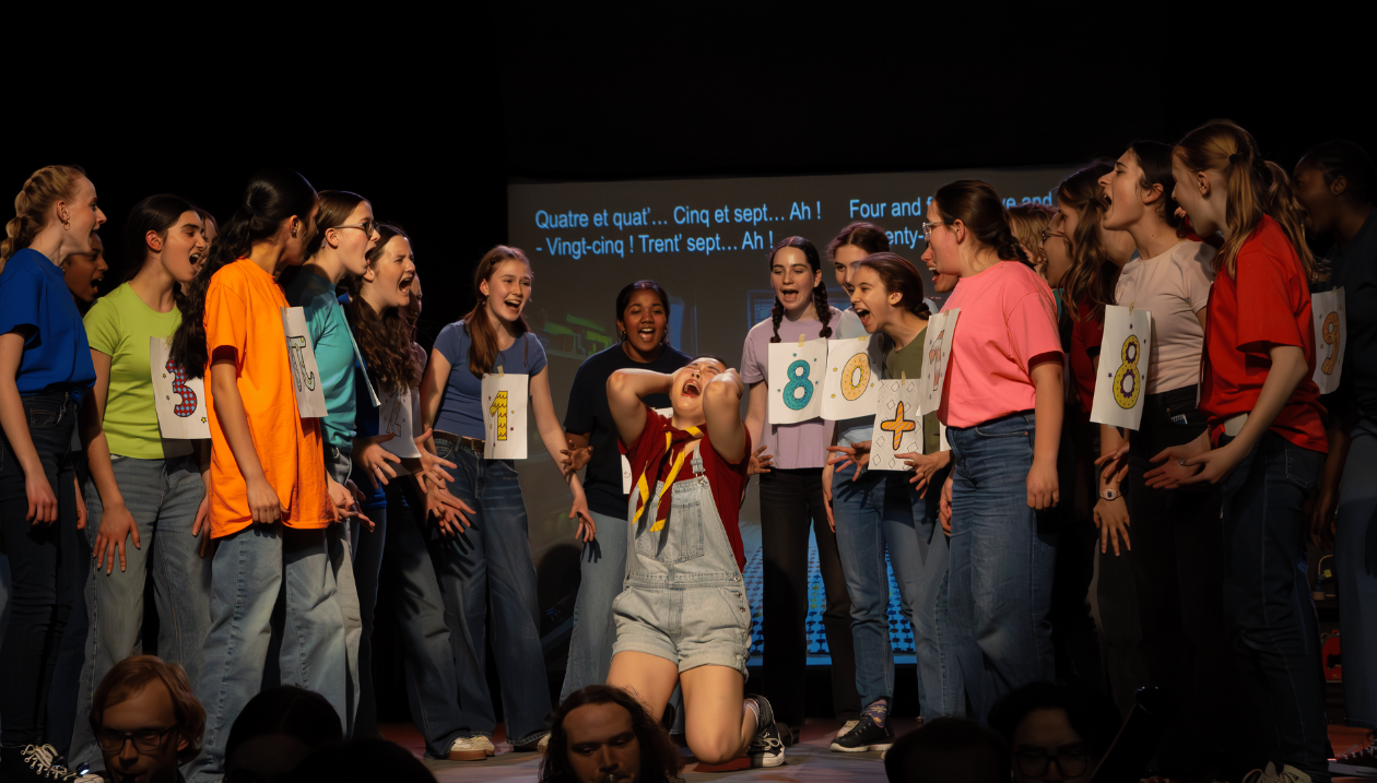 Open-mouthed performers gathered around a kneeling performer with head thrown back.