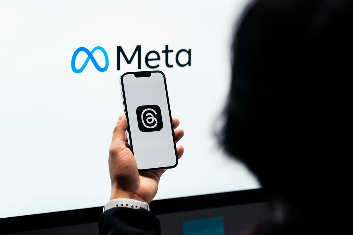 Person looking at Threads app on mobile phone with Meta logo in backdrop
