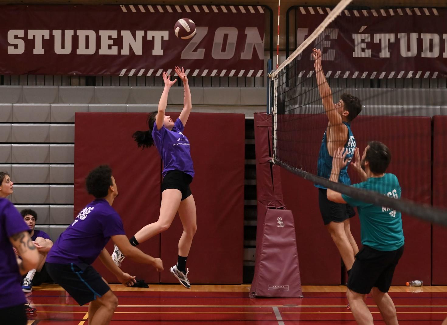 A volleyball player jumps to set the ball while opposing players jump to the net to block.