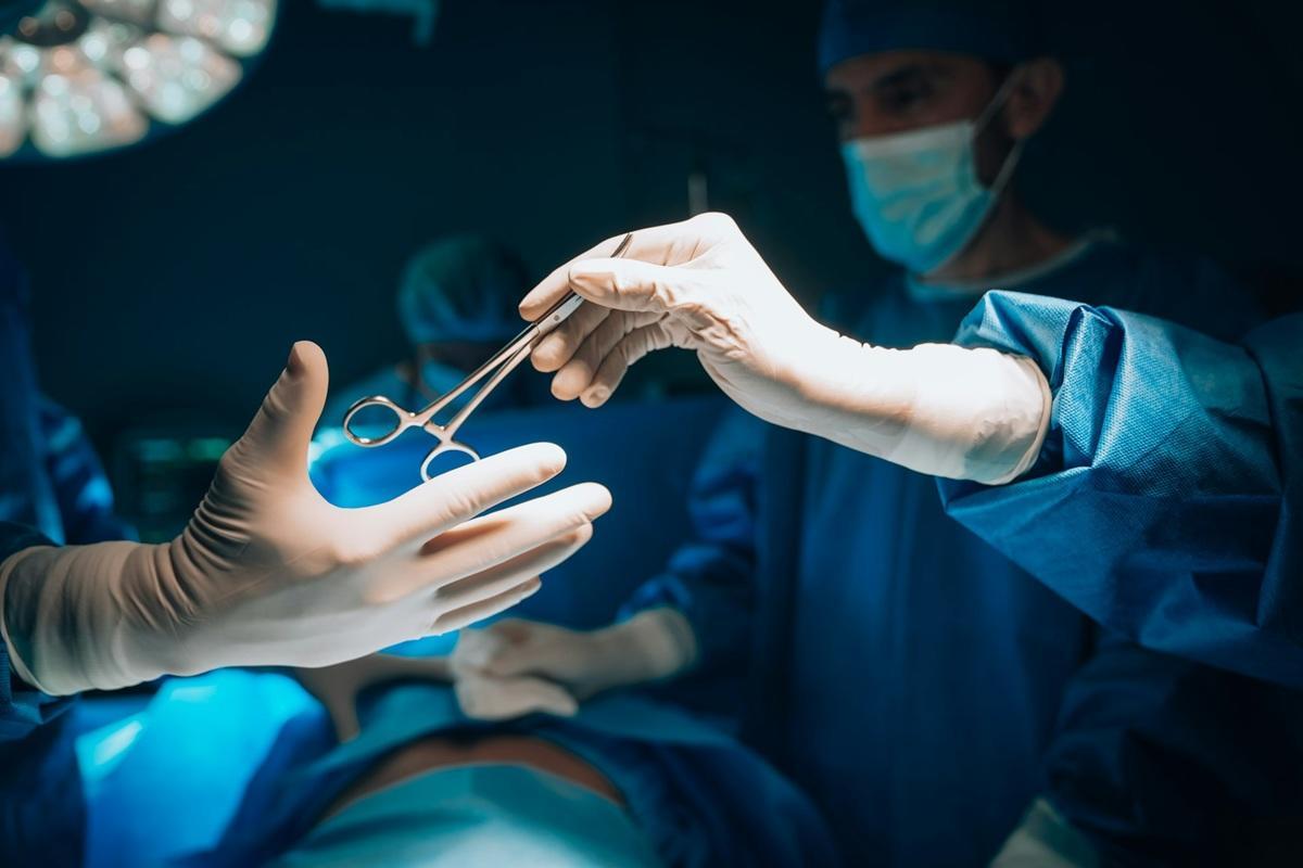 Gloved hand of a nurse giving another gloved hand a surgery tool