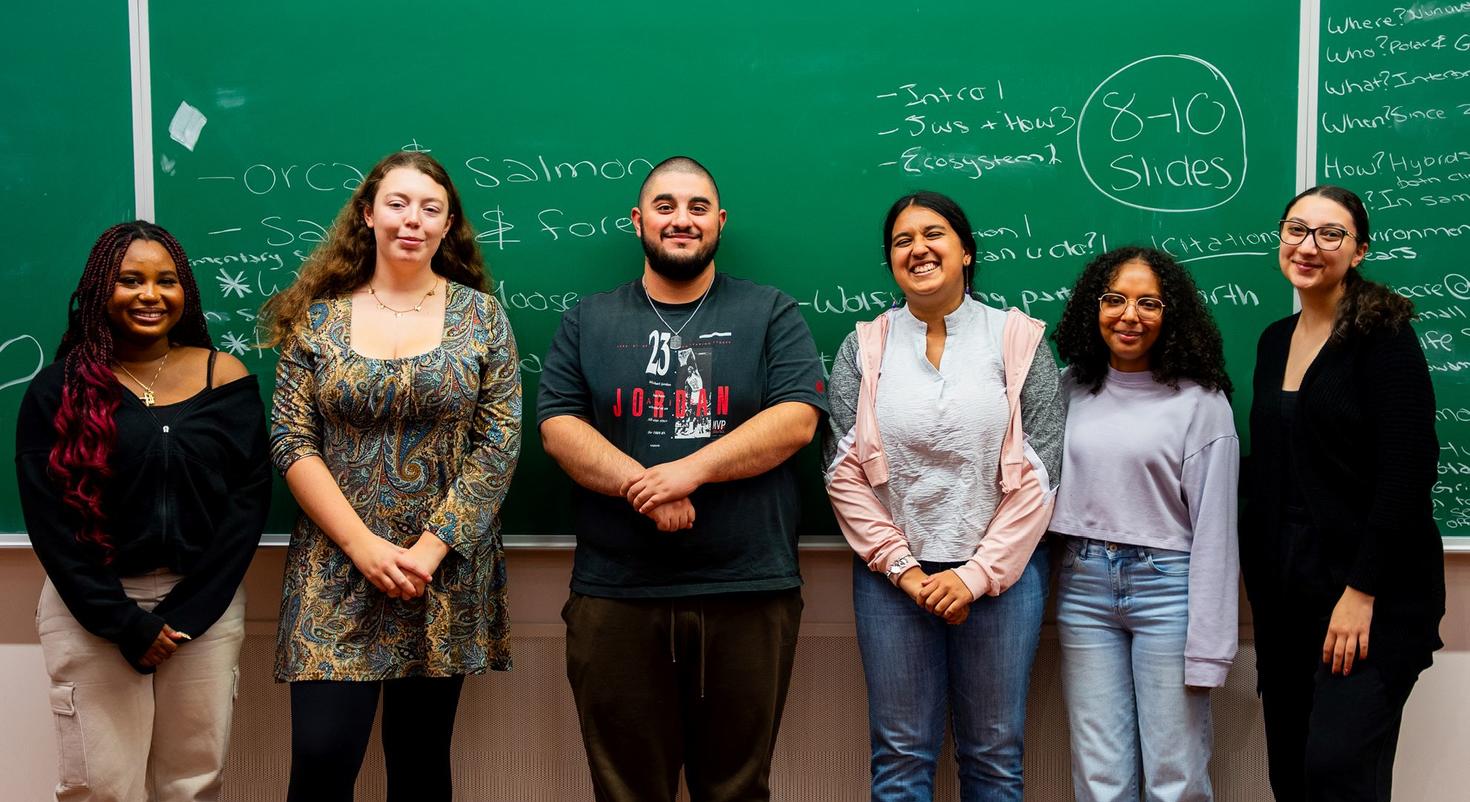 Six students who participated in a Faculty of Social Sciences interdisciplinary experiential learning challenge in 2025 stand in front of a blackboard in a classroom.