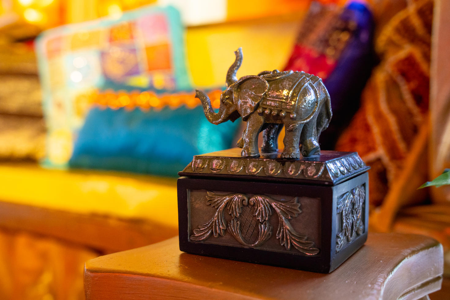 Coffret décoratif surmonté de deux éléphants en métal, devant des tissus colorés baignés d’une lumière dorée.