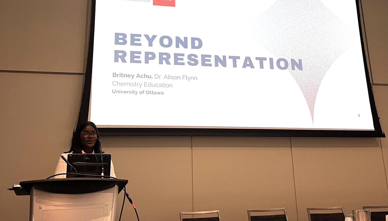 Britney Achu speaks at a conference while standing at a podium.