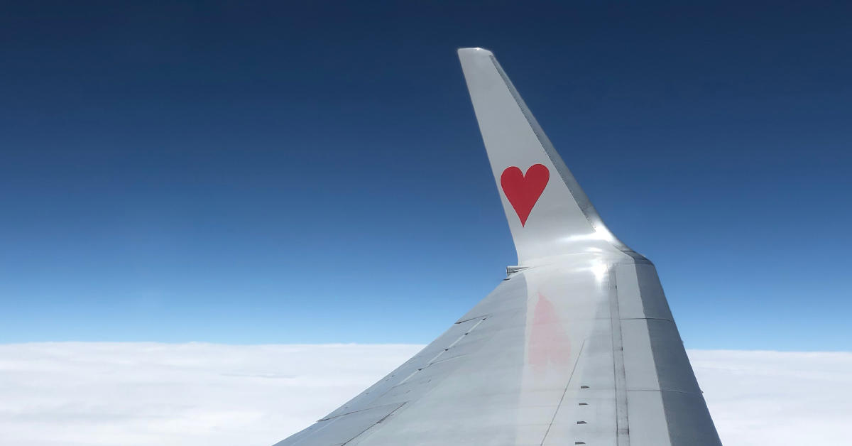aile d'avion avec un coeur rouge peint dessus, ciel bleu et nuages du point de vue des passagers