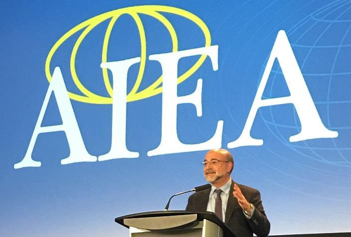Adel El Zaïm debout derrière un lutrin, sous une bannière de l’AIEA.