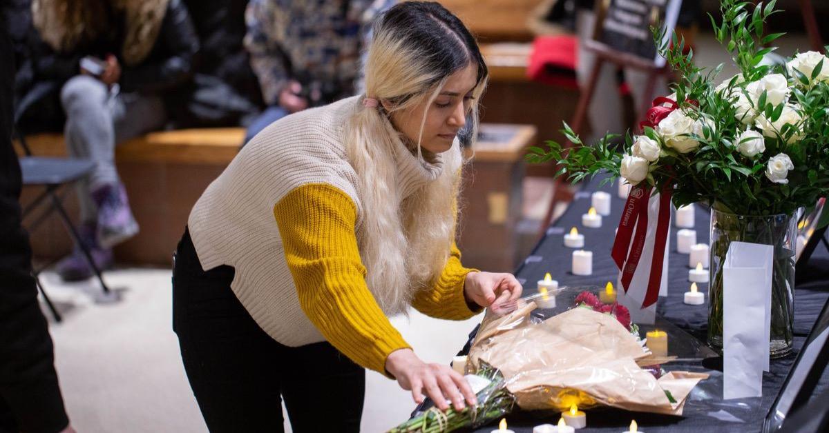 Une jeune femme dépose une gerbe de fleurs sur une table de commémoration
