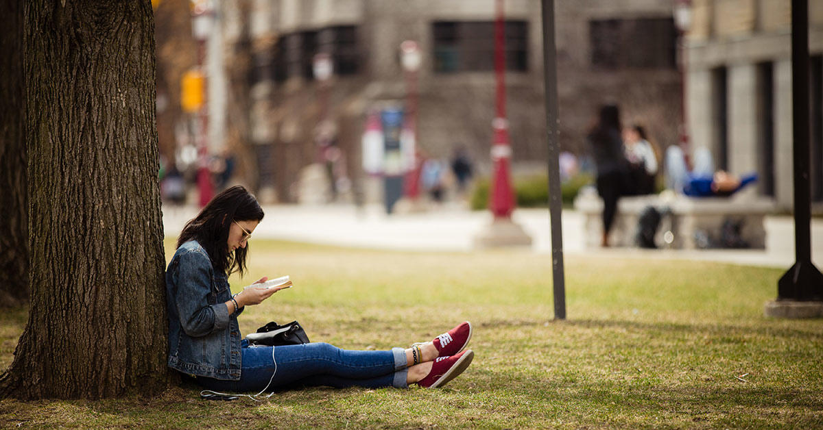 Une femme lit un livre assise sous un arbre.