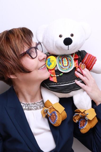 Cindy Blackstock tient près d’elle un ourson en peluche souriant qui porte des mocassins perlés.