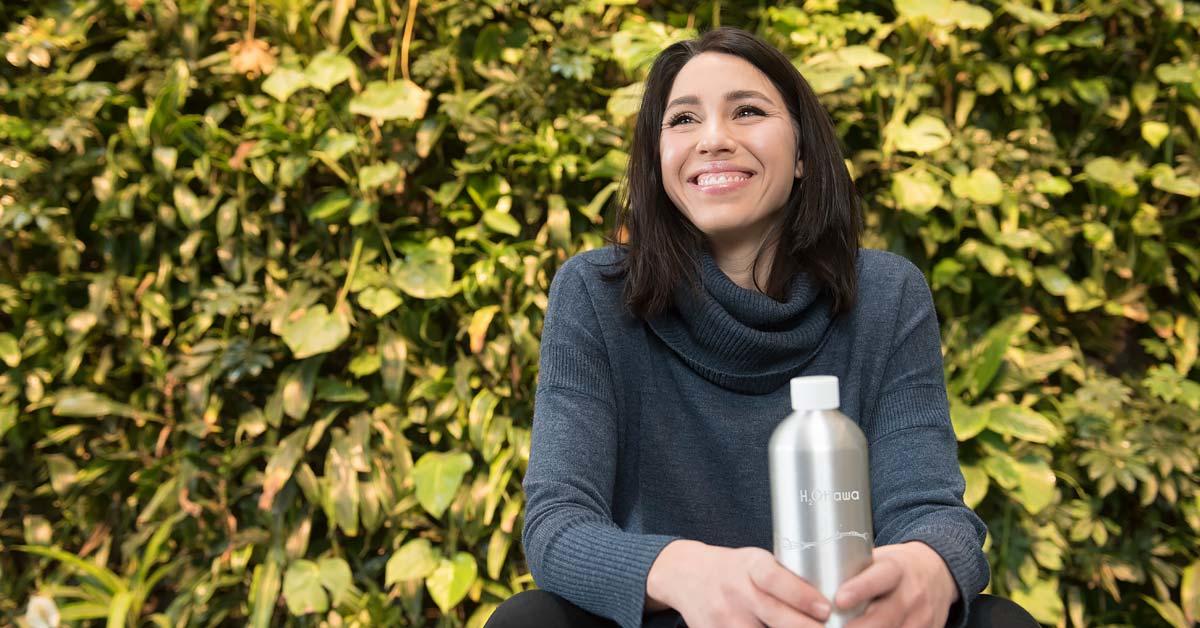 Celeste tient sa bouteille H2Ottawa devant un mur de feuillage