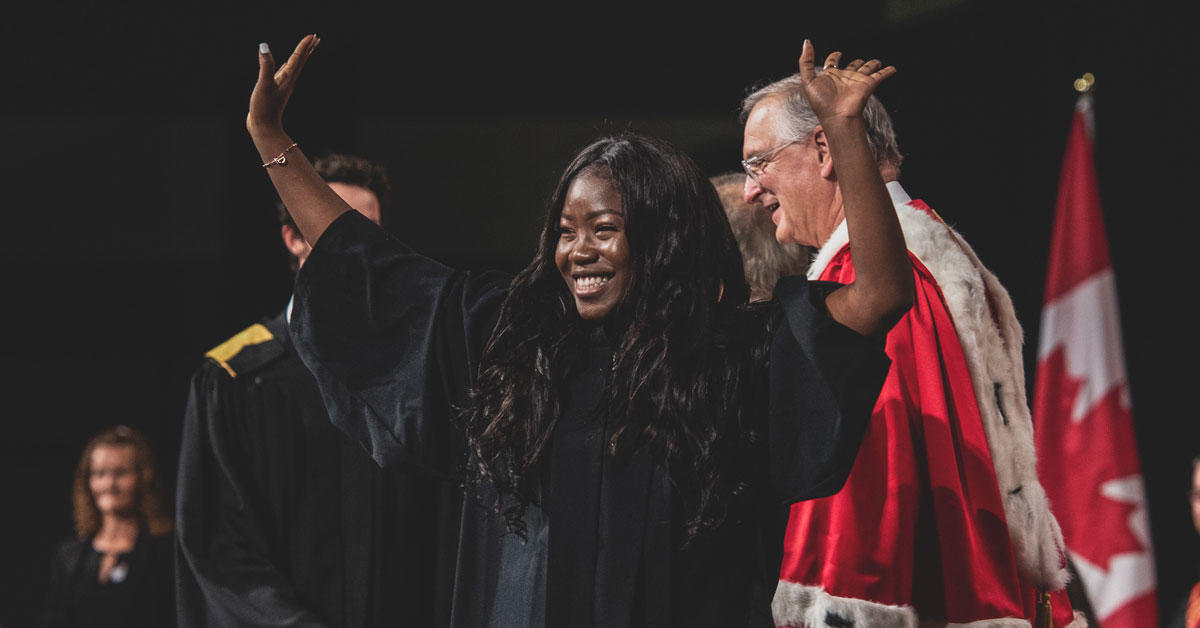 A graduating student crosses the stage at convocation, with the President in the background.