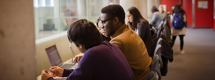 Three students look at a laptop.