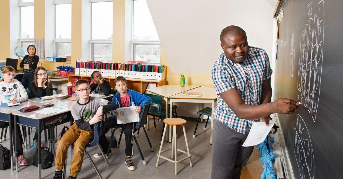 Un enseignant écrit au tableau devant des enfants assis dans une salle de classe.