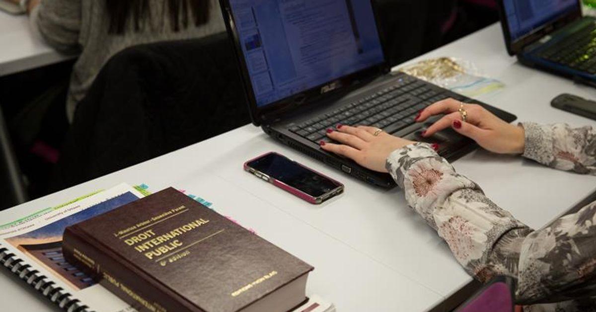 Les mains d'une femme sur le clavier d'un ordinateur portable. Un livre de droit est posé sur la table.