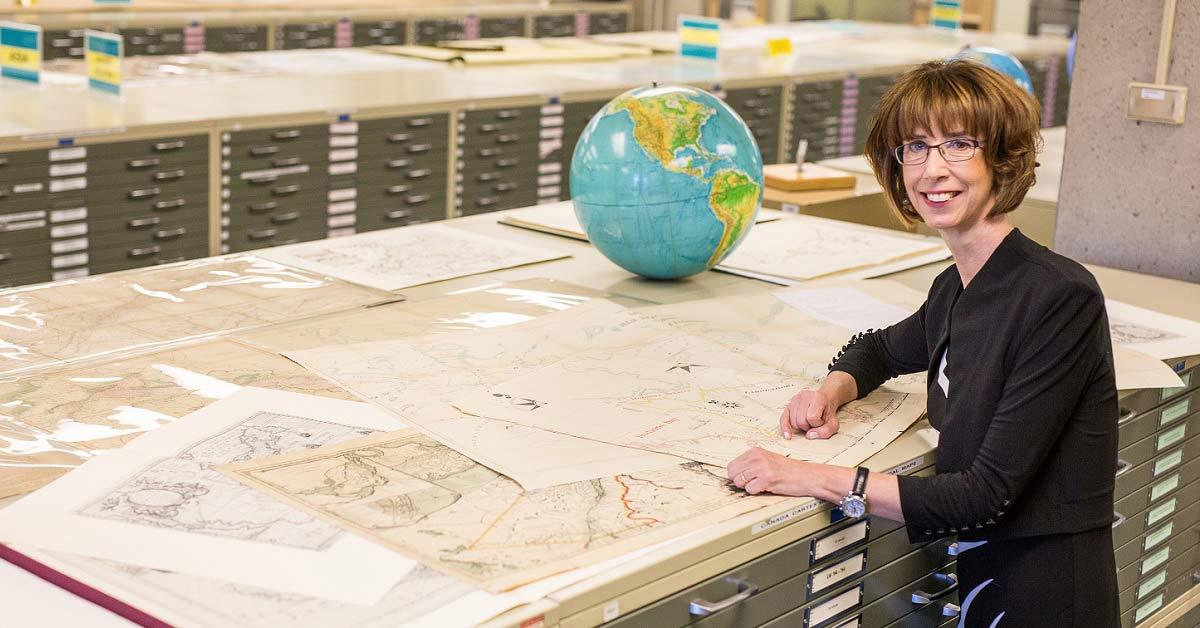 France Martineau se tient debout dans une salle d’archives de cartes du monde. 