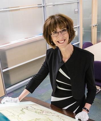 France Martineau se tient debout dans une salle d’archives de cartes du monde. 