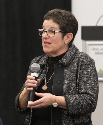 Anne Gilbert parle dans un micro qu’elle tient à la main.