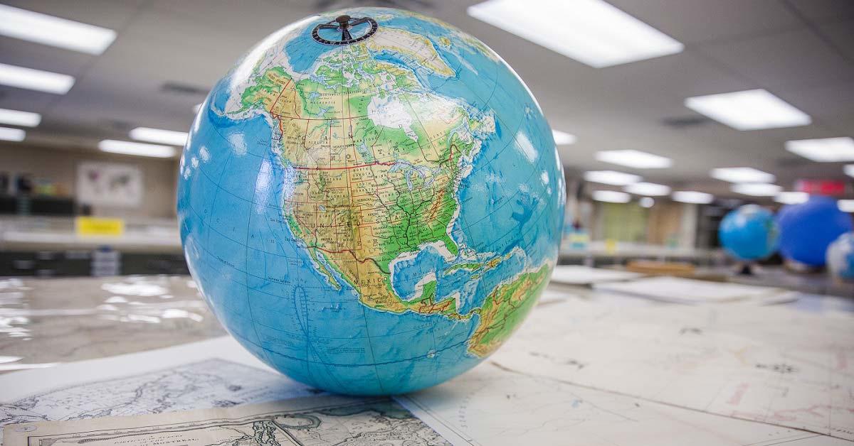 Gros plan d’un globe terrestre où l’Amérique du Nord est à l’avant-plan. On aperçoit une salle d’archives de cartes du monde en arrière-plan.