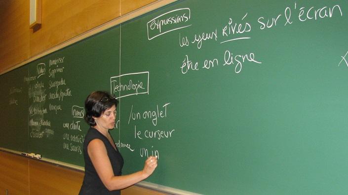 Enseignante de l’ILOB se tient devant un tableau en train d’enseigner du vocabulaire reliée aux nouvelles technologies.