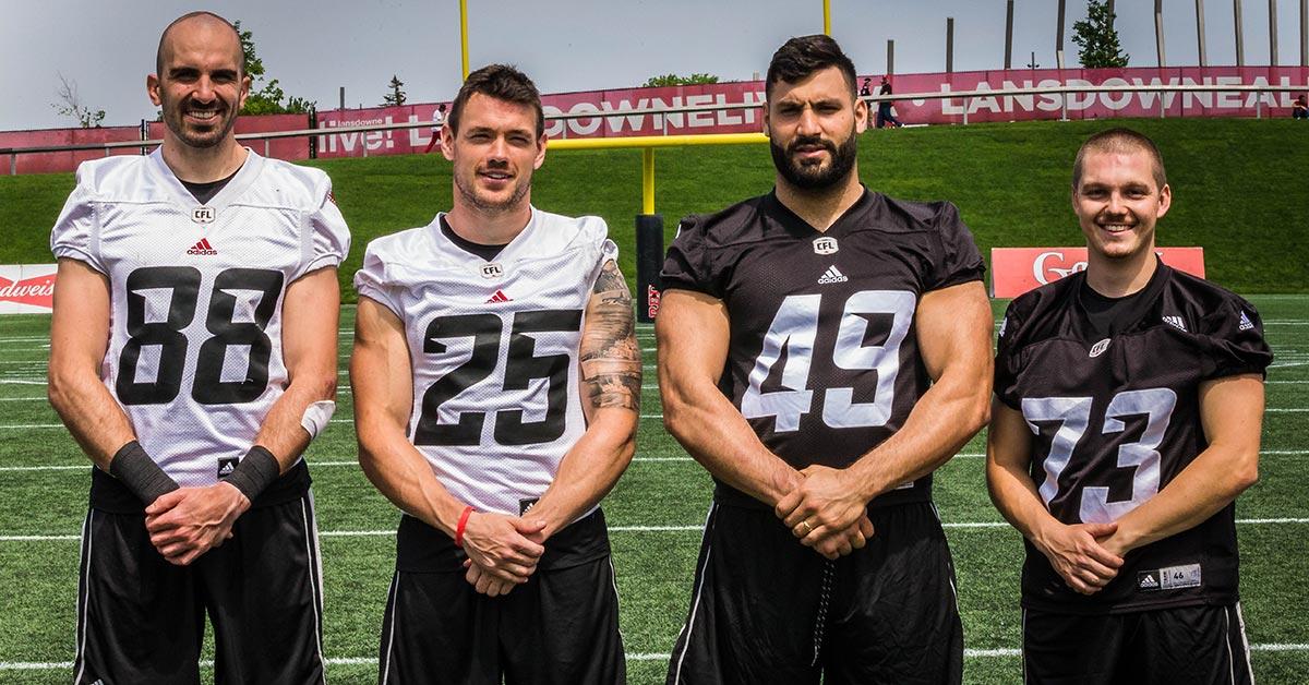 Quatre joueurs de football se tiennent côte à côte au centre du terrain.