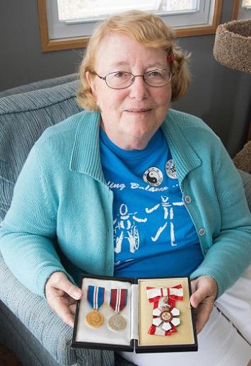 Monique Frize sits in her living room holding three medals.