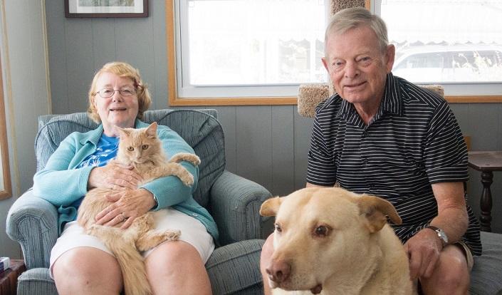 Monique and Peter Frize sit in their living room with a cat and dog.