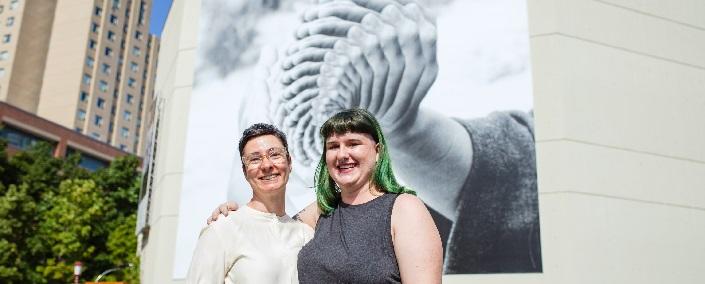 Two women smiling in front of the mural.