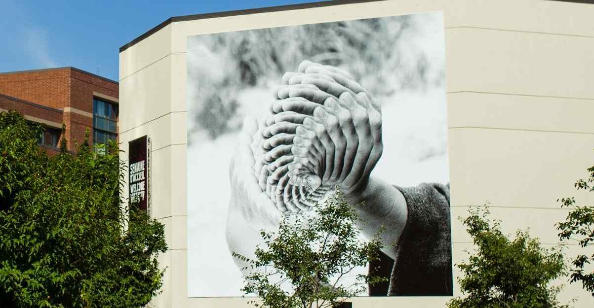 Immense toile accrochée sur le mur extérieur d'un immeuble représentant des mains, reproduites en superposition.