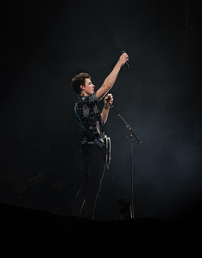 Shawn Mendes portant une guitare et levant son micro.