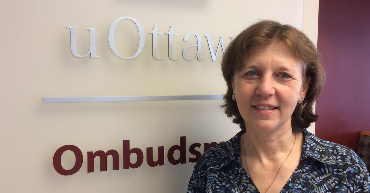 La nouvelle ombudsman de l’Université d’Ottawa, Martine Conway, pose à l’entrée de son bureau devant une enseigne sur laquelle est écrit « uOttawa | Ombudsman ».