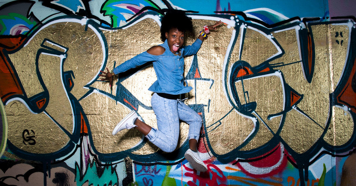 Pearline Barrett-Fraser saute en dansant devant un mur de graffitis colorés