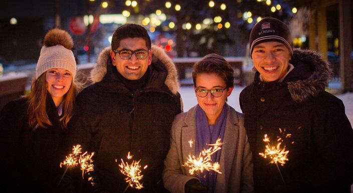 Four students bundled in winter coats hold lit sparklers.