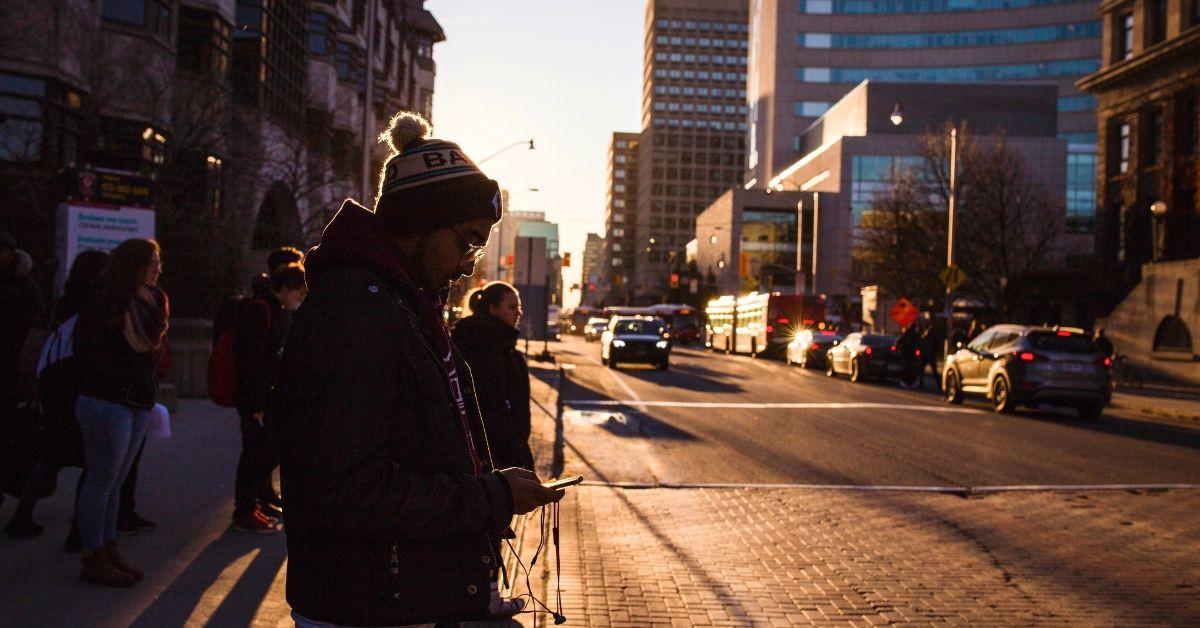 A student looks at his smart phone. Students, cars and buildings appear in the background.