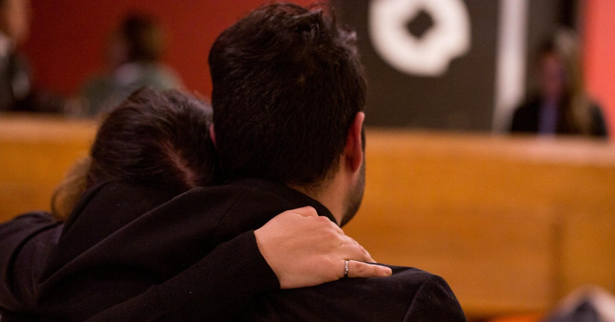 An individual has their hand on a friend's shoulder, they are facing away from the camera.