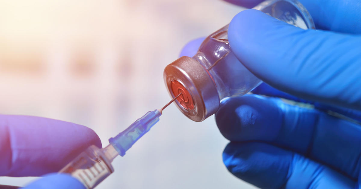 A syringe inserted into a vial of vaccine.