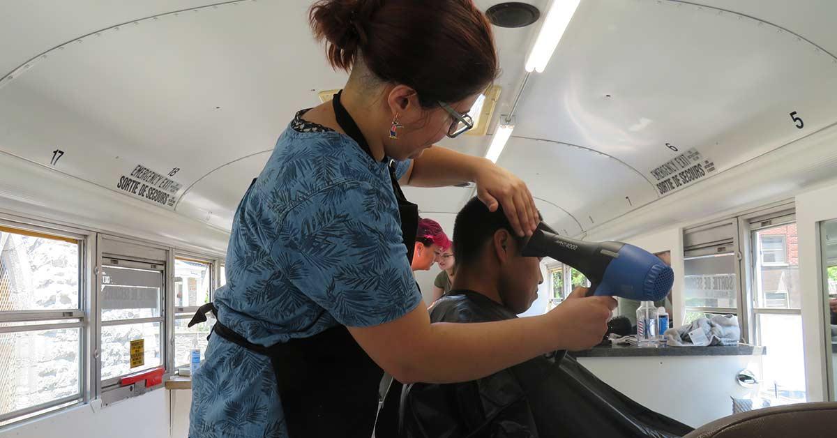 Une coiffeuse bénévole sèche les cheveux d'un usager.