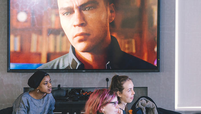 Trois étudiantes ont les yeux rivés vers l’avant; à leurs côtés, un écran où figure un personnage animé.