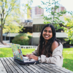 A woman sitting on a bench in front of her laptop in the middle of a park
