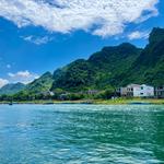 Picture of a lake surrounding a small island with habitations and mountains. Blue sky and white clouds in the background